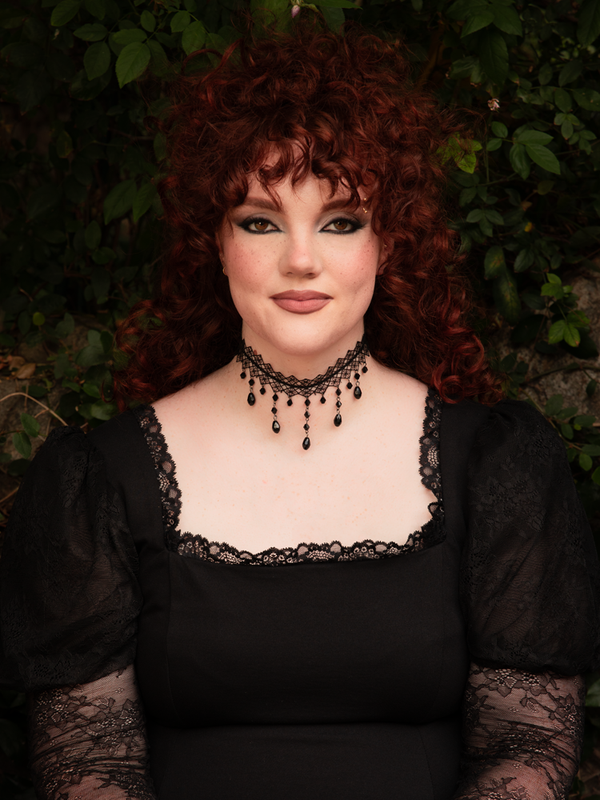 A striking gothic accessory, the Woven Choker in Black is shown adorned with faceted drop crystals that evoke a sense of antique mourning jewelry. The delicate yet dramatic woven pattern creates a silhouette of timeless dark elegance, perfect for a modern femme fatale.