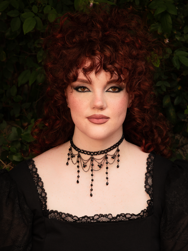 Styled against bare skin, the dangling black beads shimmer softly, evoking dark romance and baroque decadence beneath candlelit skies.
