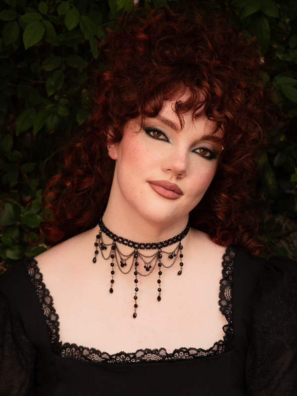 Black beads cascade from the choker like shadowed chandeliers, framing the neck in dramatic elegance and midnight allure with every subtle movement.