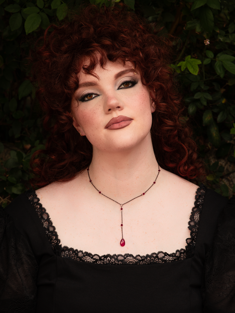 A gothic water drop necklace featuring deep red crystals suspended from a delicate chain, evoking vampiric elegance and dramatic gothic allure against dark attire.