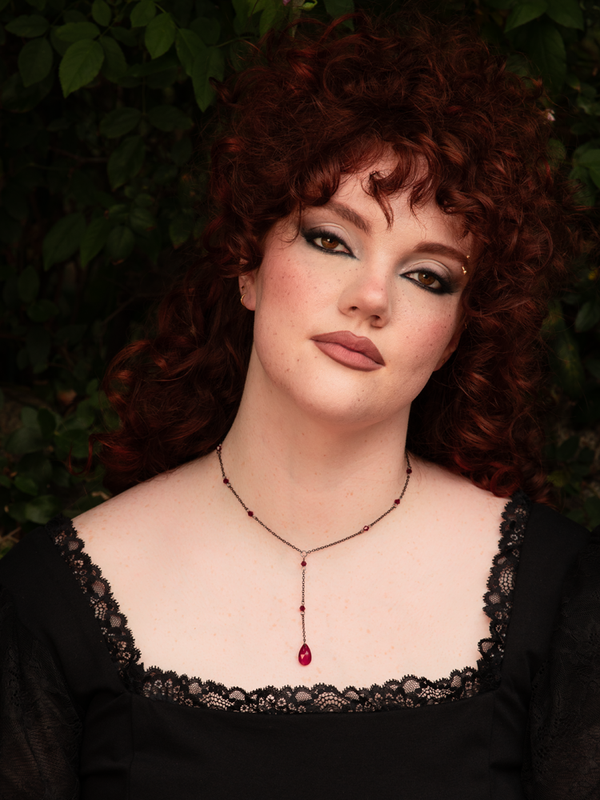 Close-up of blood-red teardrop crystals catching the light, creating a haunting gothic necklace that embodies dark romance and nocturnal sophistication.