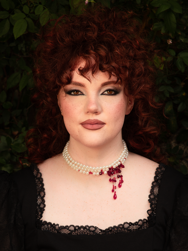 Close-up of cascading red crystals against white strings, evoking a vampiric elegance where purity meets seductive gothic drama.