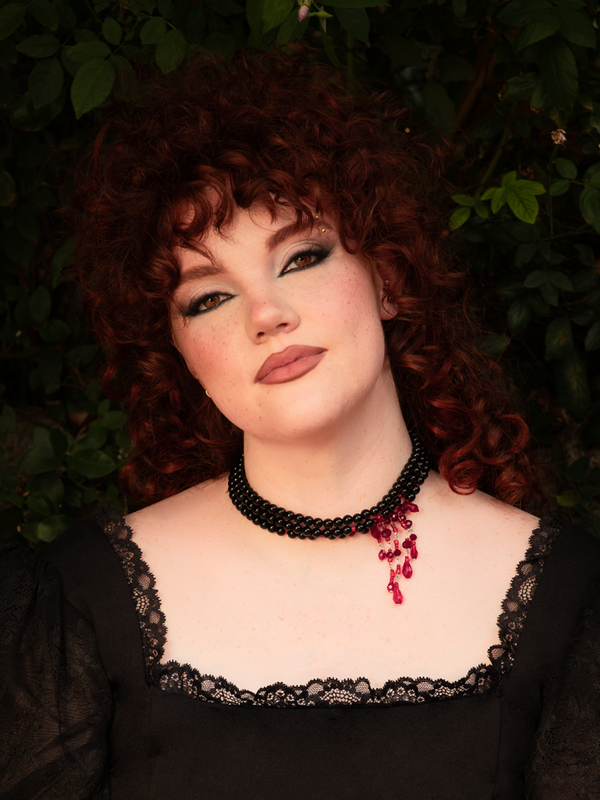 Multiple black strands wrap the neck in dark elegance as red blood crystals shimmer like forbidden rubies, creating a dramatic gothic choker with vampiric allure and statement impact.