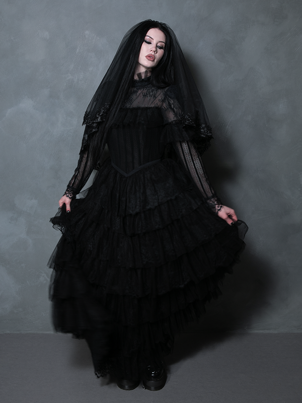 Female model draped in a sweeping black romantic goth gown radiating macabre sophistication.