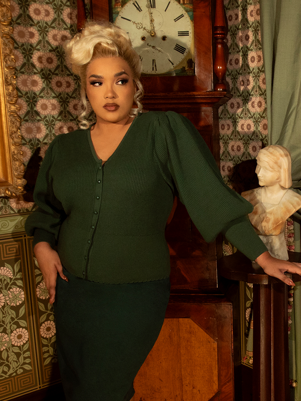 A nod to Victorian refinement, this fitted knit cardigan in hunter green is adorned with elegant pleating and ornate buttons, creating a timelessly polished silhouette.

