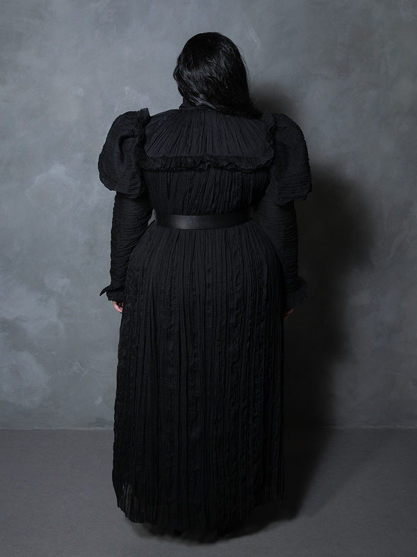 A gorgeous representation of dark romance, a female model wears a flowing black dress designed with quintessential gothic glamour.