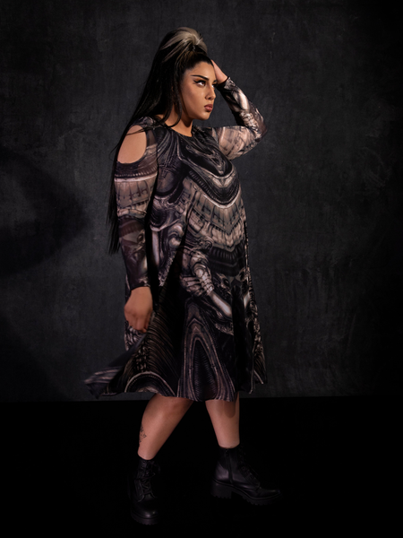 Jyoti Kaur standing to the side while wearing the Alien™ Xenomorph Trapeze Dress in front of a dark background.