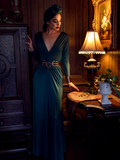 Aliza, looking down in a gothic style home, models the Art Deco ruched gown in green from La Femme En Noir.