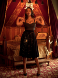 Chelsea, standing with her hands on her shoulders in a moody boudoir, models the A Spider's Kiss skirt from La Femme En Noir.