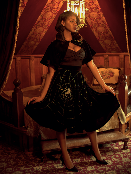 Chelsea, standing in a moody boudoir with her hands on her skirt, models the A Spider's Kiss skirt from La Femme En Noir.