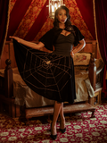 Chelsea, standing in a moody boudoir, models the A Spider's Kiss skirt from La Femme En Noir.