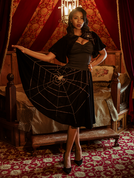 Chelsea, standing in a moody boudoir, models the A Spider's Kiss skirt from La Femme En Noir.
