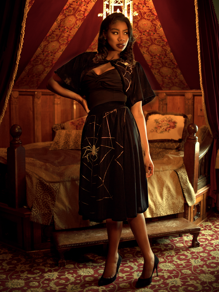 Chelsea, standing in a moody boudoir, models the A Spider's Kiss skirt from La Femme En Noir.
