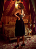 A back shot ofChelsea, looking over her shoulder in a moody boudoir, models the A Spider's Kiss skirt from La Femme En Noir.