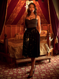 Chelsea, standing in a moody boudoir, models the A Spider's Kiss skirt from La Femme En Noir.