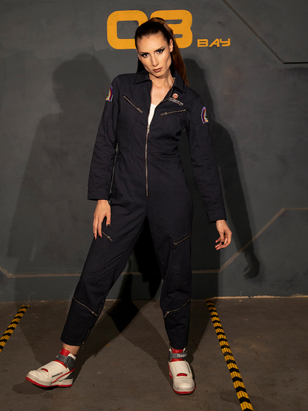 KJ standing and looking into the camera with one leg outstretched while modeling the ALIEN Ripley Flight Suit in Navy from La Femme en Noir. 