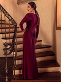 A back shot of Aliza, standing on a staircase with her hand on her hip, models the Art Deco ruched gown in crimson from La Femme En Noir.