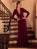 A full length shot of Aliza, standing on a staircase with her hands on her waist, models the Art Deco ruched gown in crimson from La Femme En Noir.