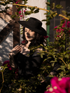Slightly obscured by shadows, female model wears the Bolero Hat in Black to accent her gothic black dress. All items sold by goth clothing brand La Femme en Noir.