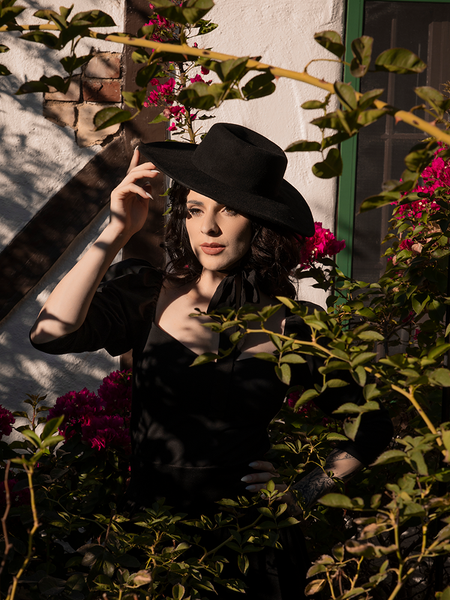 Model looks off camera while wearing the Bolero Hat in Black from La Femme en Noir.
