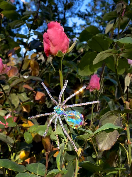 The Spider Baby Rhinestone Spider Brooch pictured against a pink rose garden.