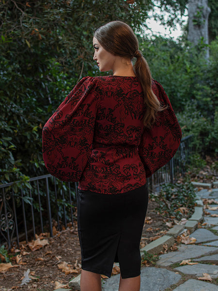 A back shot of Aliza with her hands on her hips modeling the Georgette wrap top in gorgon print paired with a black pencil skirt.