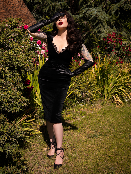 Covering her face from the glare of the sun, Micheline Pitt models elbow length vegan leather gloves to complement the Baudelaire Wiggle Dress in Black she's wearing.
