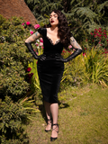 Standing with her hands on her hips, Micheline Pitt soaks in the rays of the sun while wearing the Baudelaire Wiggle Dress in Black.