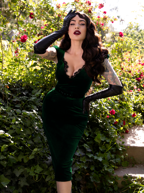 Micheline Pitt posing while wearing the Baudelaire Wiggle Dress in Hunter Green in a rose garden.