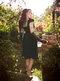 Micheline Pitt turned away from the camera to show off the back of the Baudelaire Swing Dress in Hunter Green from gothic clothing brand La Femme en Noir.