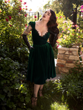 Full length shot of Micheline Pitt wearing the Baudelaire Swing Dress in Hunter Green with complementary elbow length leather gloves.