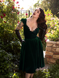 Micheline Pitt poses in a sunny rose garden while wearing the Baudelaire Swing Dress in Hunter Green from goth clothing company La Femme en Noir.