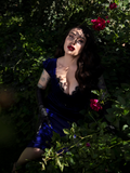 Micheline Pitt, sitting in a shady spot hidden from the sun, wears the Baudelaire Wiggle Dress in Midnight Blue from goth clothing company La Femme en Noir.
