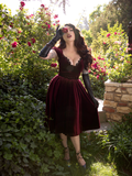 Holding a rose up to her face, Micheline Pitt mysteriously gazes into the camera while modeling a gothic style dress.