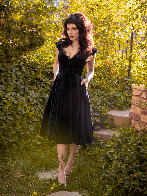 Stephanie stares off to the side while tucking her hands into the pockets of her Baudelaire Swing Dress in Black from La Femme en Noir.