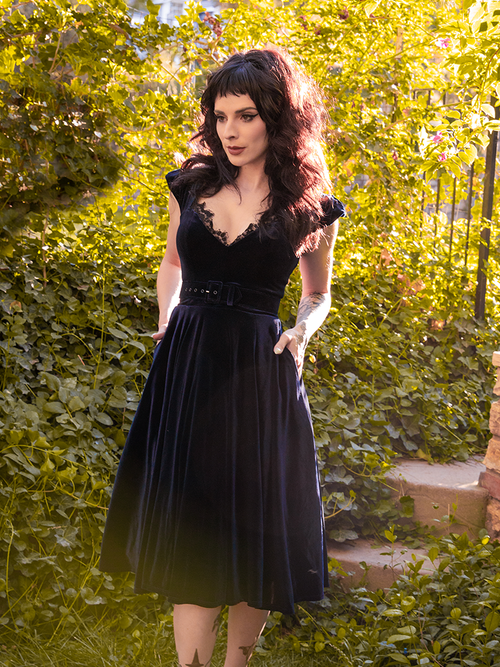 Stephanie stands in a sun-soaked garden while wearing the Baudelaire Swing Dress in Black from gothic dress company La Femme en Noir.
