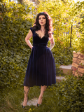 Posing with her arms bent and hands on the backs of her hips, Stephanie models the Baudelaire Swing Dress in Midnight Blue from La Femme en Noir.