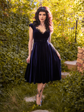 Looking directly at the camera, Stephanie gently pulls out the skirt on the Baudelaire Swing Dress in Midnight Blue from La Femme en Noir.