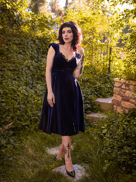 The Baudelaire Swing Dress in Midnight Blue modeled by Stephanie standing in a lush, green garden.
