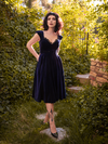 With her hands tucked into the pockets of the Baudelaire Swing Dress in Midnight Blue, Stephanie looks intensely into the camera while modeling the Baudelaire Swing Dress in Midnight Blue from goth dress company La Femme en Noir.