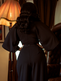 A back shot of Rachel standing in a beautiful home with her hands on her hips modeling the Bauhaus top in black from La Femme En Noir.