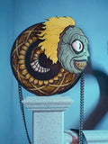 The BEETLEJUICE™ Beetlesnake Crossbody Bag sitting on a concrete railing post against a pale blue background.