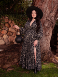 Radiating beauty in a garden setting, the brunette model elegantly models the Belladonna Maxi Dress in Cottage Witch Toile Print from the gothic clothing brand La Femme en Noir.