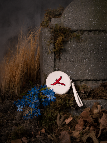 Sat against a tombstone, the Sleepy Hollow Bird Cage Thaumatrope Wristlet is photographed next to some blue flowers. 