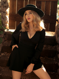 A Blonde Micheline Pitt modeling the Bishop Blouse in Black while standing in front of her garden gate.