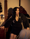 Micheline Pitt sat on the side of her bed while wearing the Bishop Blouse in Black.