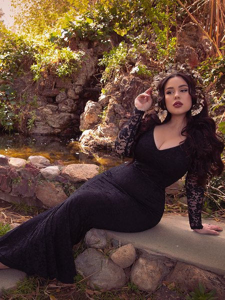 Rachel Sedory sitting on a stone rock wall while wearing a black gothic dress and flower headdress. 