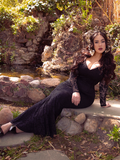 Rachel Sedory sitting in front of a pond while wearing a black goth retro dress.