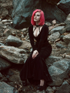 A full length shot of Mackenzie sitting on rocks and modeling the Black Marilyn gown in black paired with a harness.