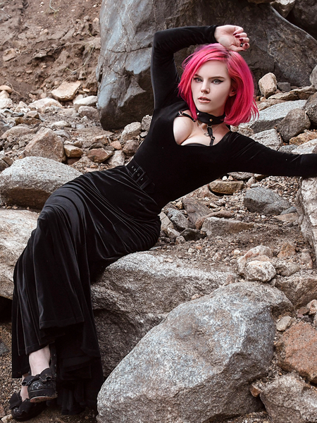 Mackenzie sitting on a rocky area modeling the Black Marilyn gown in black paired with a harness.